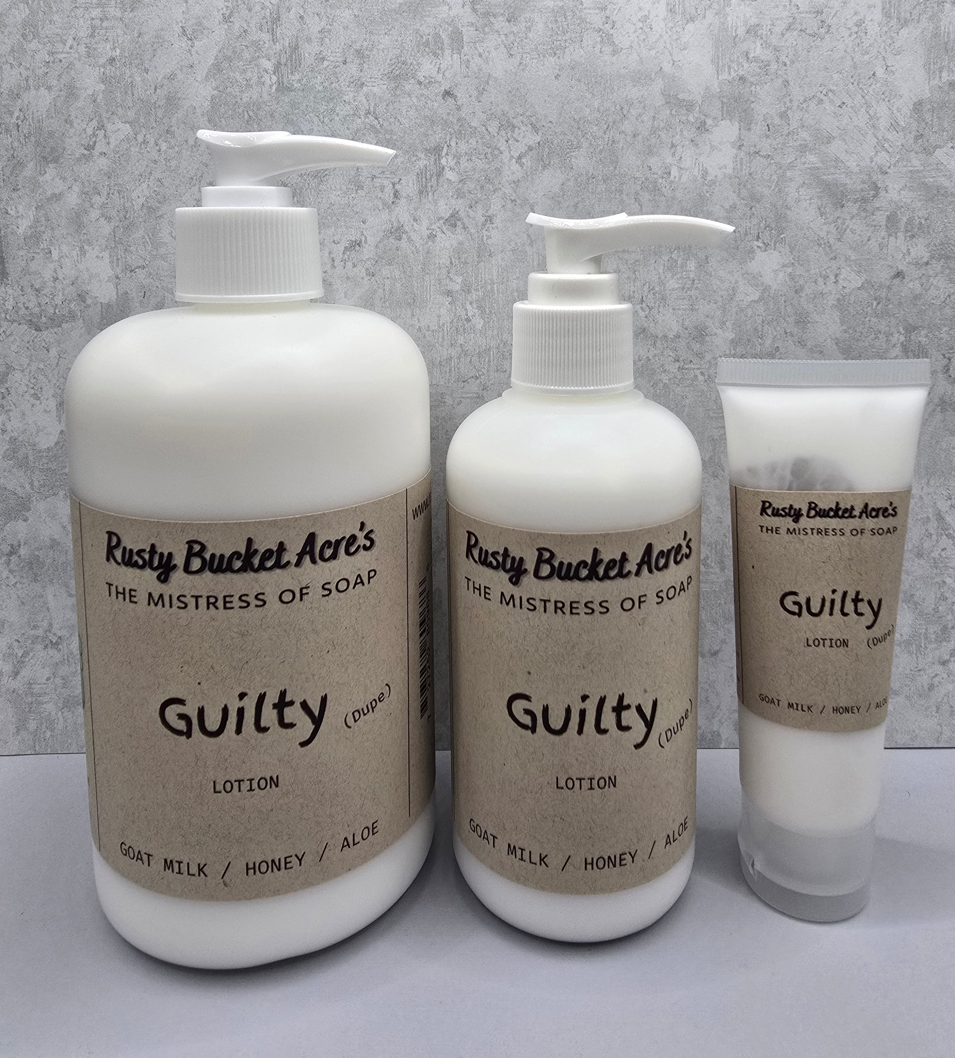 Two bottles and a tube of Rusty Bucket Acres Guilty Dupe lotion on a gray background