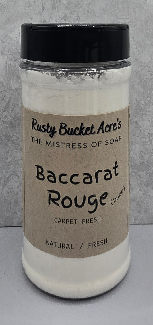 A clear plastic jar of Rusty Bucket Acre's 'Baccarat Rouge Dupe' carpet fresh soap, filled with white lather and topped with a black lid, set against a gray textured background. 