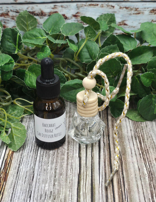 Bottle of essential oil and car diffuser refills on a wooden surface with green leaves in the background