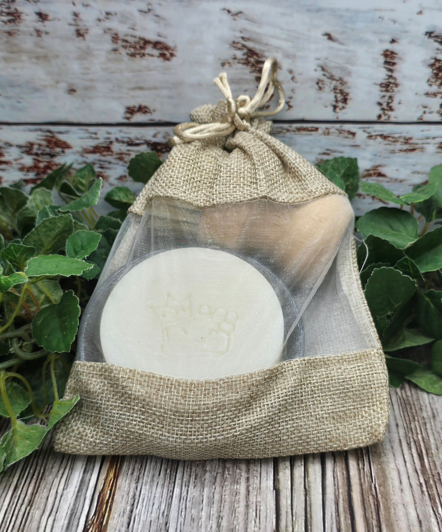Two round white objects in a burlap drawstring bag on a wooden surface with greenery.