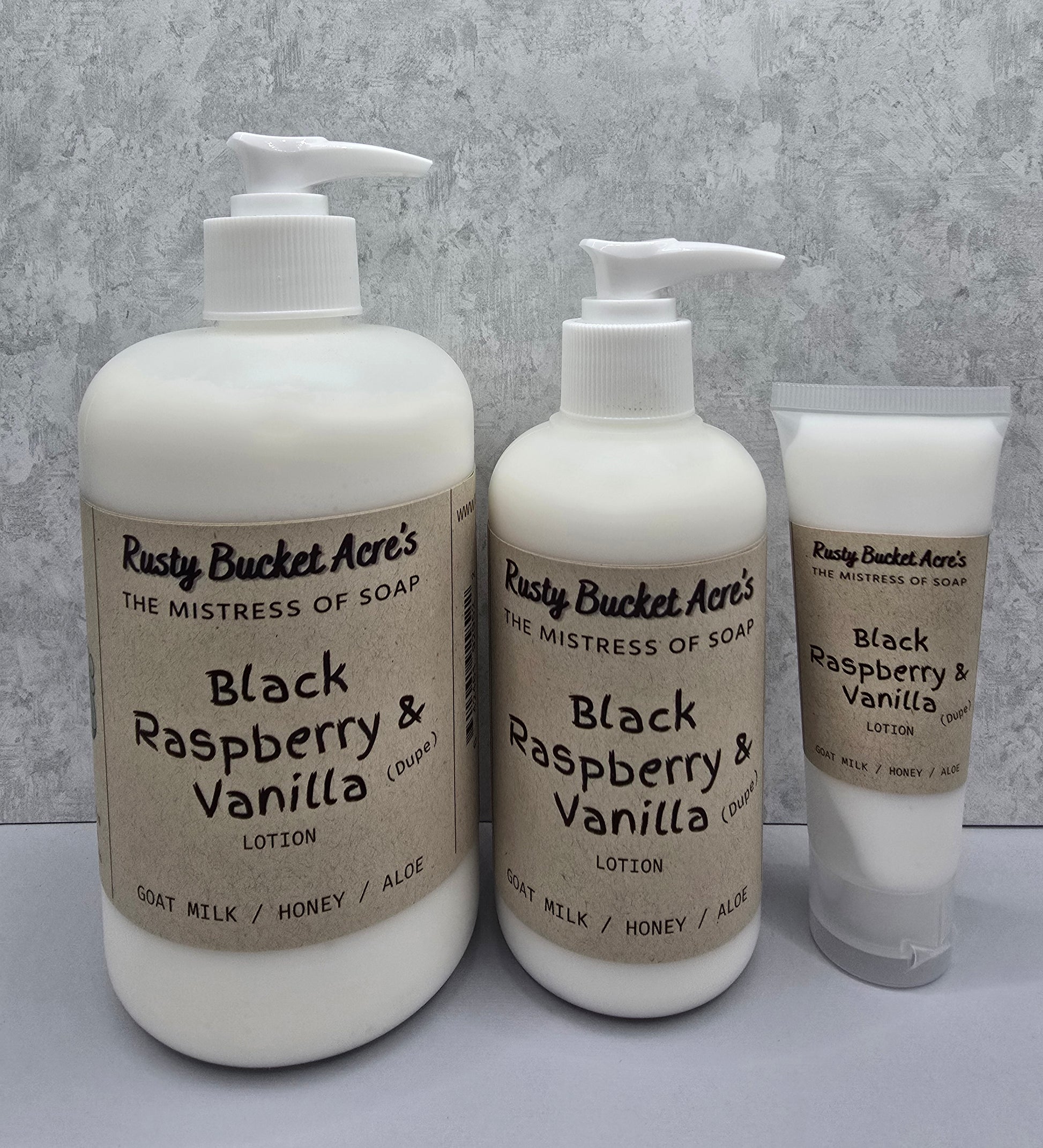 Two bottles and a tube of Rusty Bucket Acres Black Raspberry & Vanilla Dupe lotion on a gray background