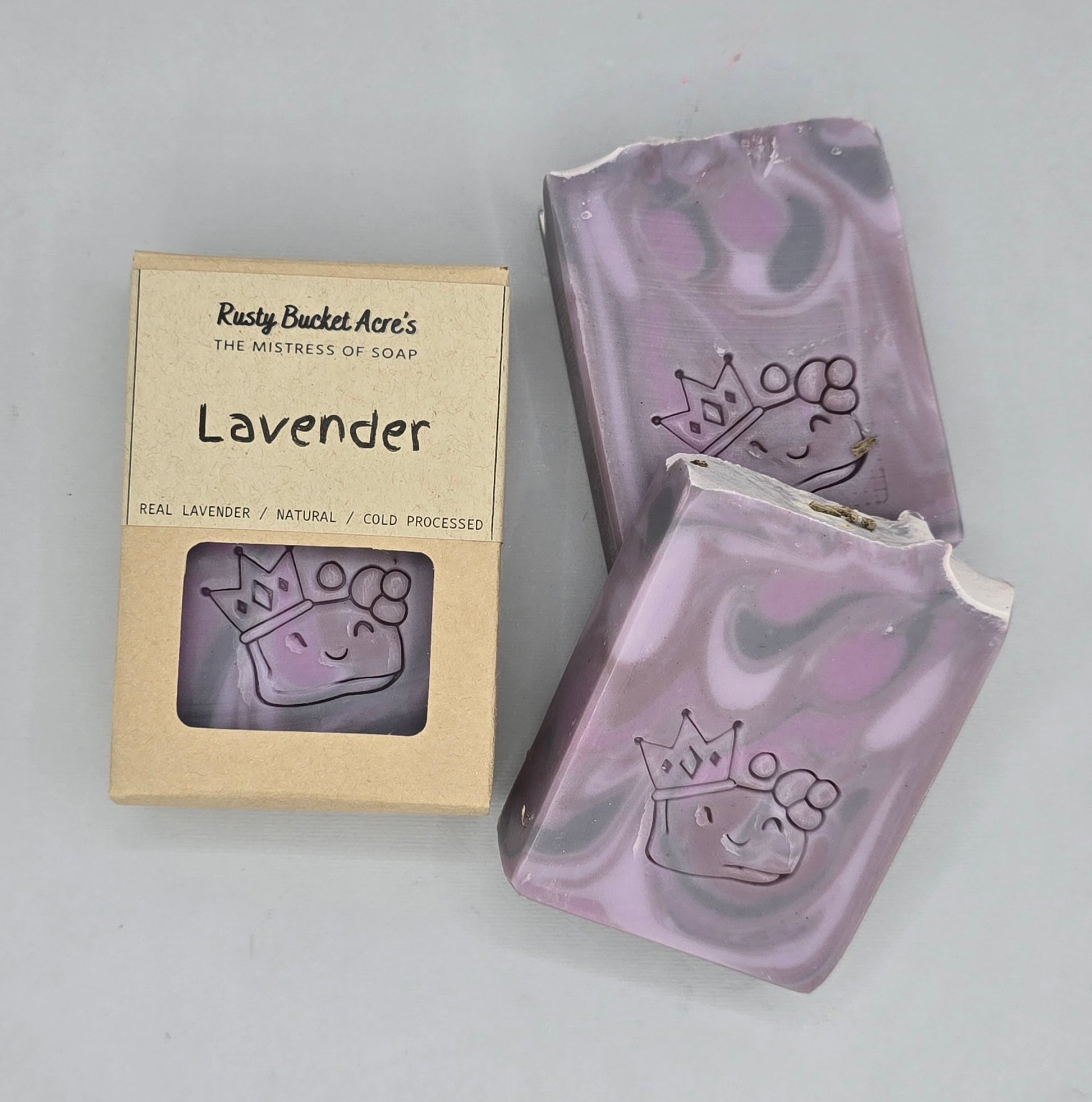 Lavender artisan soap bars with a crown and flower design, shown next to their kraft paper packaging box labeled 'Rusty Bucket Aro's Lavender'.