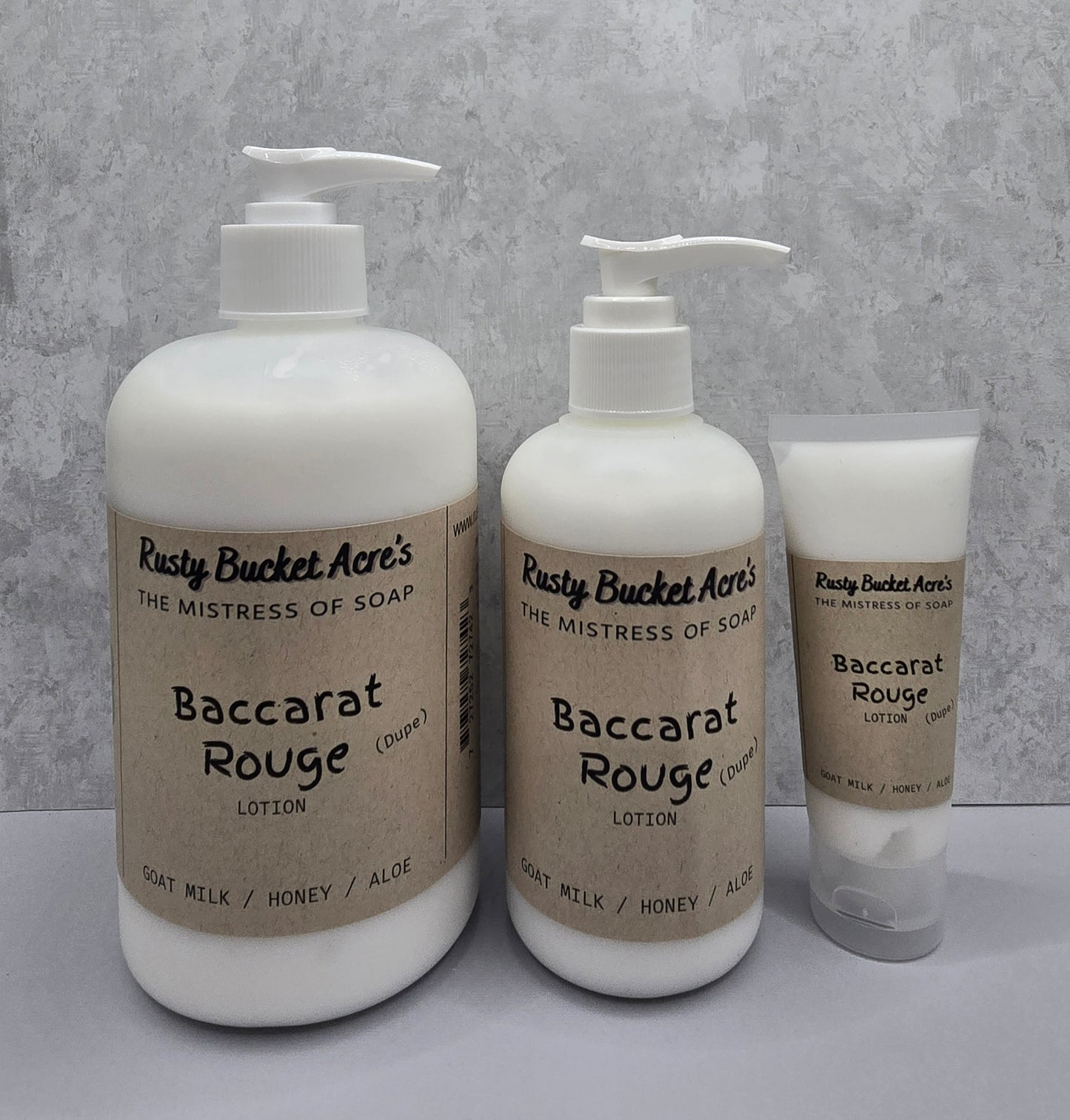 Two bottles and a tube of Rusty Bucket Acres Baccarat Rouge Dupe lotion on a gray background