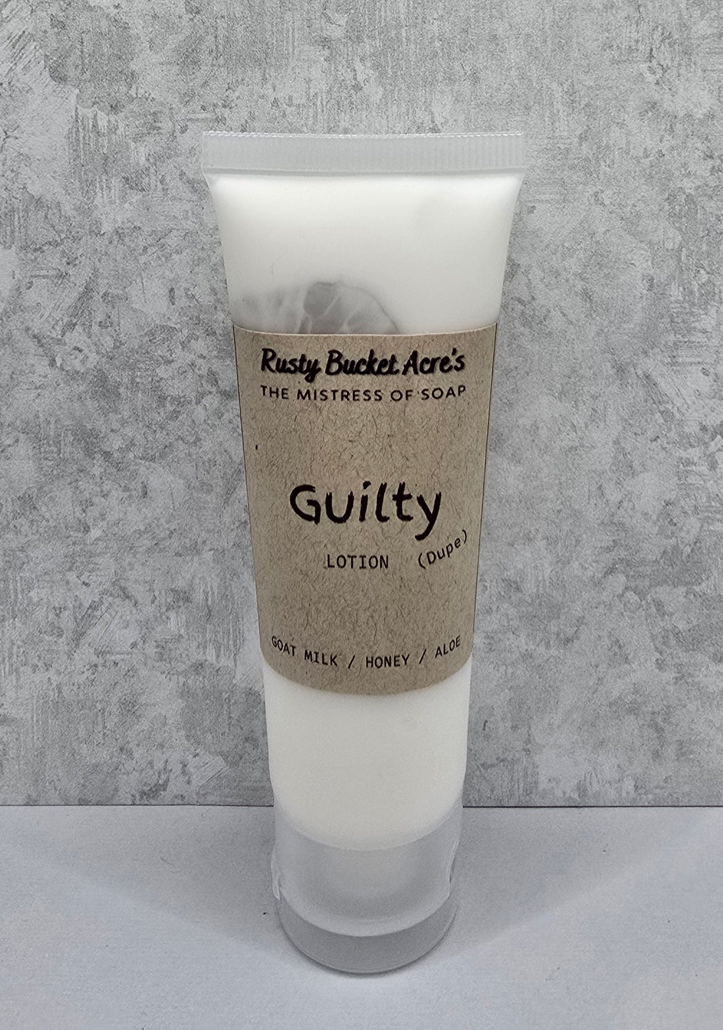 Tube of Guilty Dupe lotion with a kraft paper label on a gray background