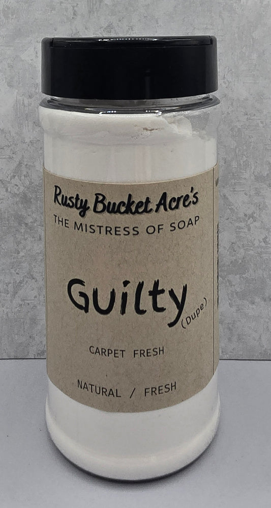 A white plastic jar of Rusty Bucket Acre's 'Guilty (Dupe)' carpet fresh soap with a black lid and a beige kraft paper label, set against a gray textured background.