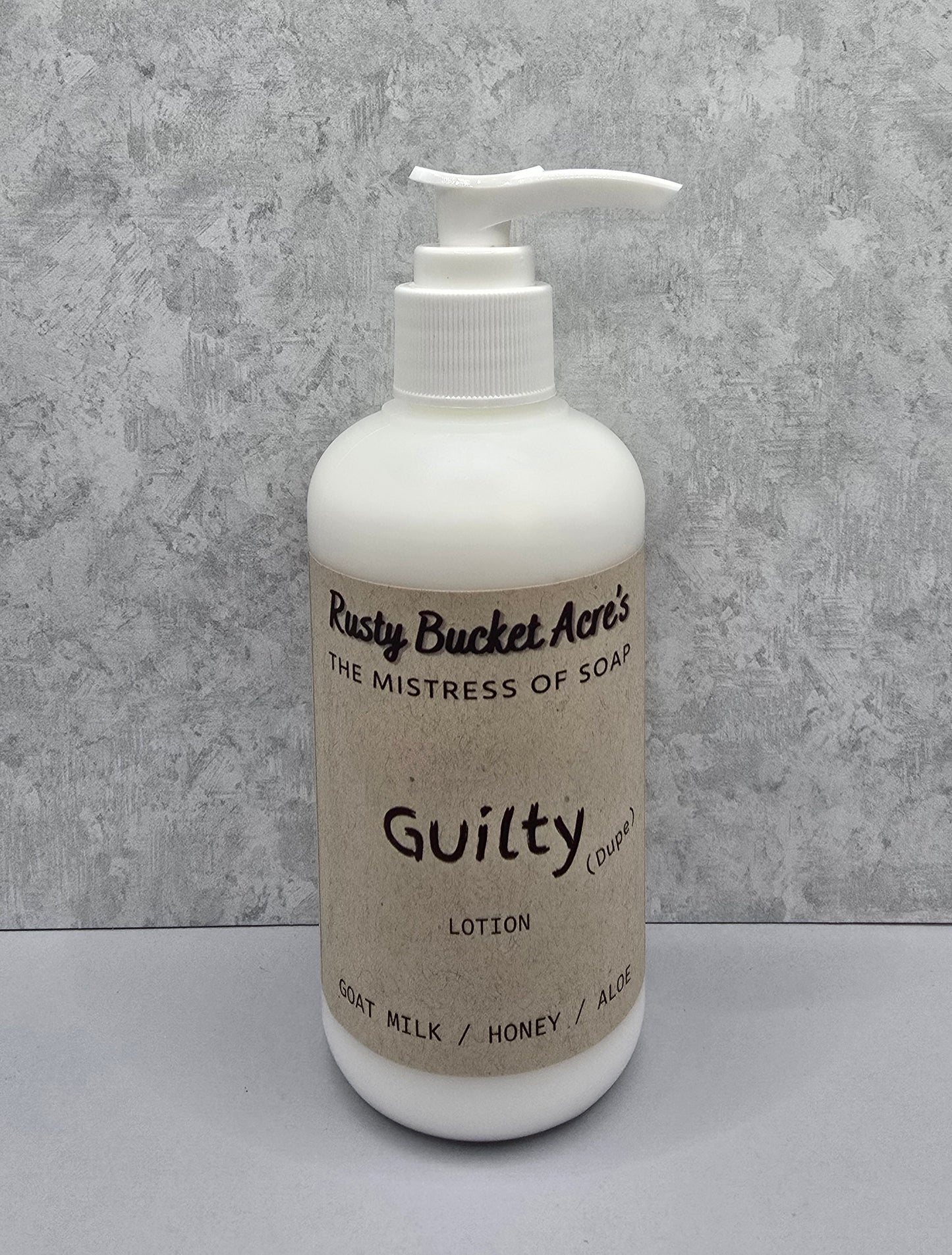 Lotion bottle with 'Rusty Bucket Acres Guilty Dupe' label on a gray background