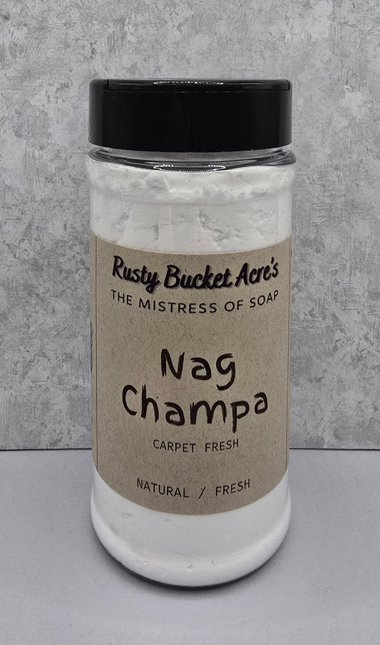 A clear plastic jar of Rusty Bucket Acre's Nag Champa carpet fresh scent with a black lid and a beige paper label, set against a textured gray background.