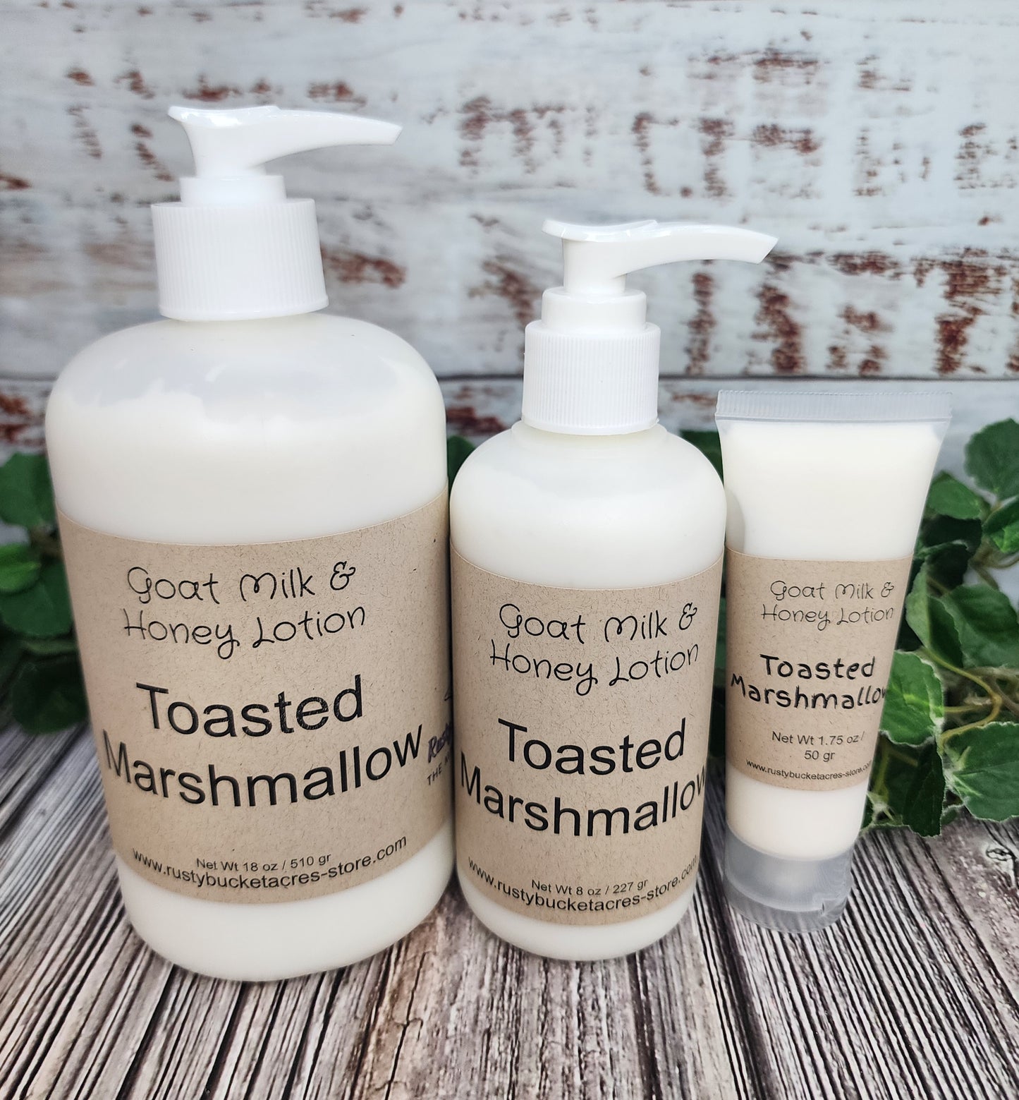 Three bottles of 'Goat Milk & Honey Lotion' with 'Toasted Marshmallow' flavor on a wooden surface.