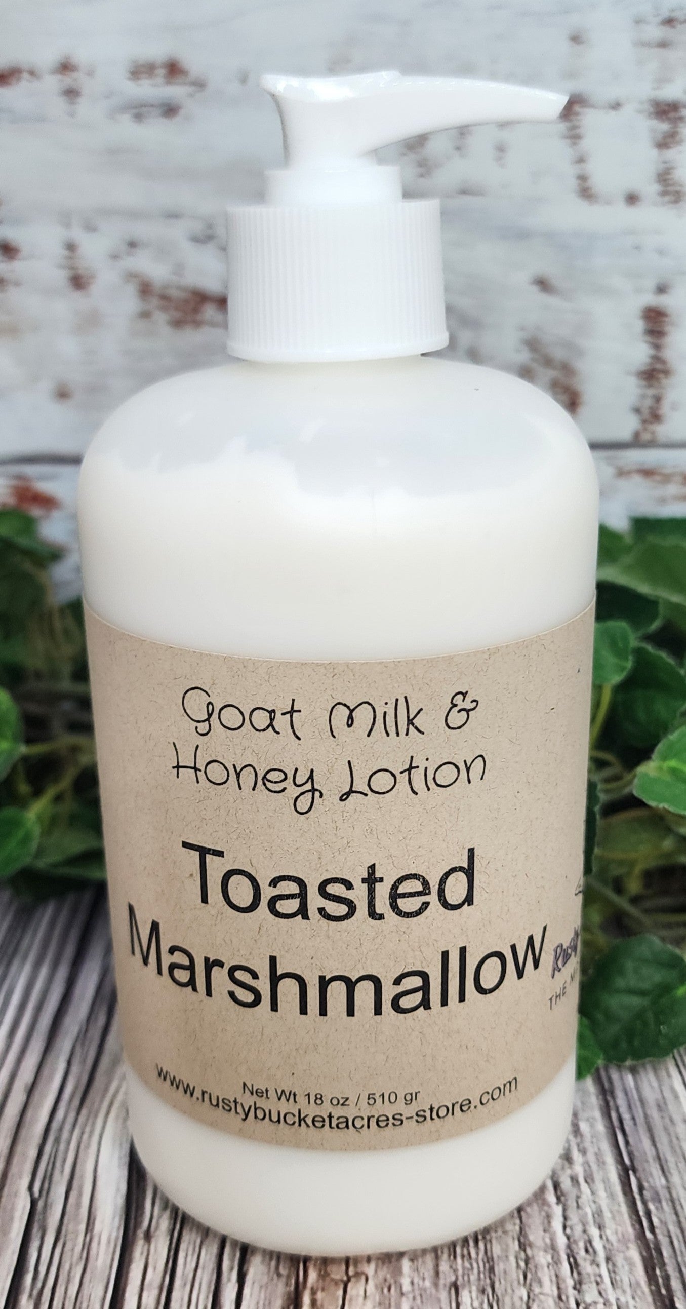 Bottle of Goat Milk & Honey Lotion labeled 'Toasted Marshmallow' on a wooden surface with a rustic background.
