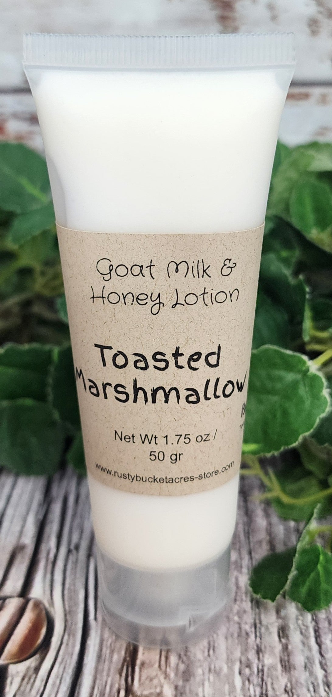 Goat Milk & Honey Lotion tube labeled 'Toasted Marshmallow' on a wooden surface with greenery.